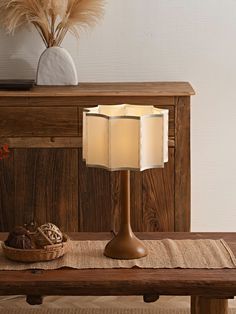 a table lamp sitting on top of a wooden bench next to a basket and vase