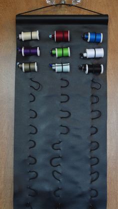 an assortment of thread spools are displayed on a black wall hanging with wine glasses