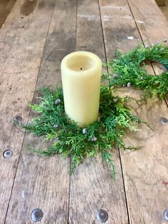 a white candle sitting on top of a wooden table next to a green plant wreath