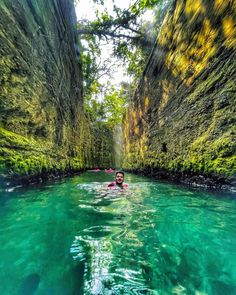 a man swimming in the middle of a river surrounded by green cliffs and trees on both sides