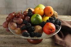 a glass bowl filled with assorted fruit on top of a wooden table