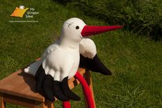 a stuffed stork sitting on top of a wooden chair with red legs and feet