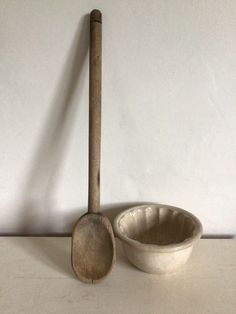 an old wooden spoon next to a white bowl on a table with a long stick sticking out of it