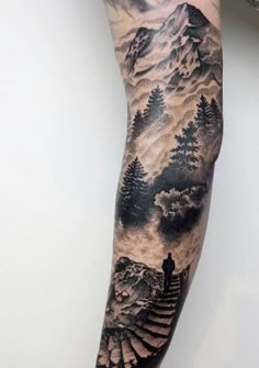 a person with a tattoo on their arm is standing in front of mountains and trees