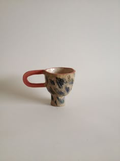 a ceramic cup sitting on top of a white table next to a red handled spoon