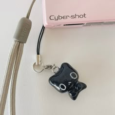 a black cat keychain sitting on top of a white table next to a pink camera