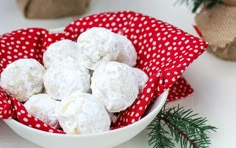 a white bowl filled with snowball cookies on top of a red and white cloth