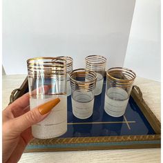 a person is holding a glass with an orange substance in it and some glasses on a tray