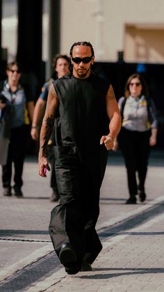 a man walking down the street in black pants and a tank top with tattoos on his arm