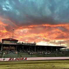 the sun is setting at an empty race track as people watch from the bleachers