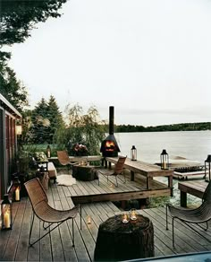 an outdoor deck with chairs, tables and a fire pit on the water's edge