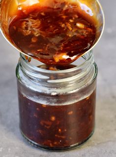 a jar filled with sauce sitting on top of a counter next to a wooden spoon