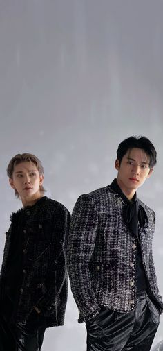 two young men standing next to each other in front of a white wall wearing black clothing