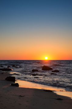 the sun is setting over the ocean with rocks in the foreground and water on the beach