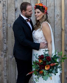 a bride and groom standing next to each other in front of a wooden fence with flowers