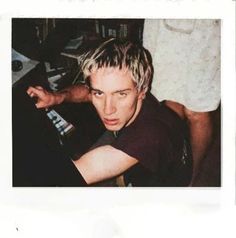 a young man with blonde hair sitting in front of a keyboard and looking at the camera