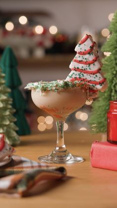 a glass filled with some kind of drink on top of a table next to christmas trees