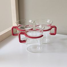 three glass cups sitting on top of a white counter next to a window sill