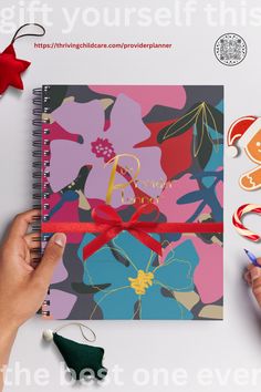 a hand holding a red ribbon on top of a spiral notebook covered in colorful flowers