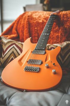 an orange electric guitar sitting on top of a couch