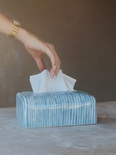 a person's hand reaching for a tissue on top of a blue box