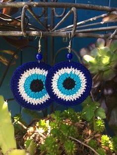 a pair of blue and white crocheted earrings hanging from a plant