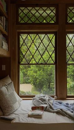 a bed sitting in front of a window next to a book shelf filled with books