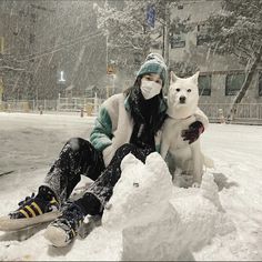 a woman sitting in the snow with her dog and wearing a face mask while it is snowing