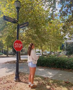 a woman standing next to a stop sign on the side of a road in front of a lamp post