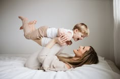 a woman laying on top of a bed holding a small child in her arms while they both look at each other