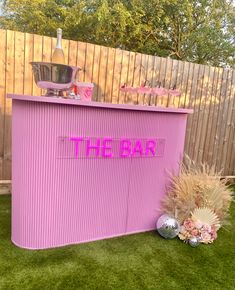 there is a pink bar in the grass with flowers and decorations around it on the lawn