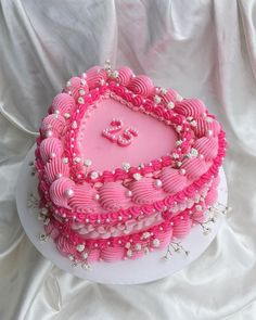 a heart shaped cake with pink frosting and pearls on it's sides, sitting on a white surface