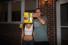 a man and woman standing next to each other in front of a brick building holding boxes