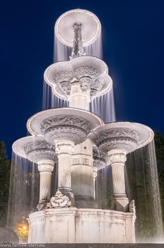 three tiered water fountain in front of trees at night with lights shining on it