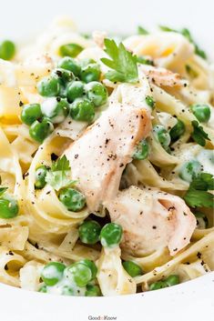 a white bowl filled with pasta and meat covered in green onions, peas and cream sauce