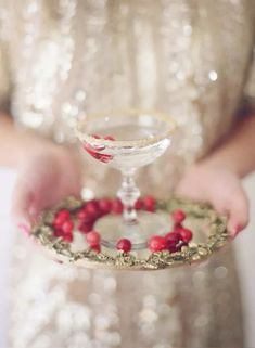 a woman holding a small glass plate with cranberries and gold trimmings