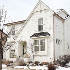 a white brick house with snow on the ground and trees in front of it,