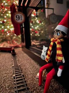 an elf is sitting on the train tracks in front of a christmas tree and window