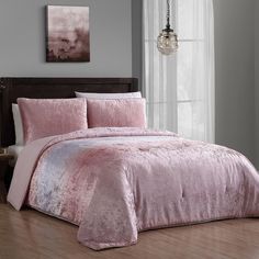 a bed with pink comforter and pillows in a room next to a lamp on a table