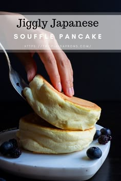 someone is cutting into some pancakes on a plate with blueberries and blackberries next to it