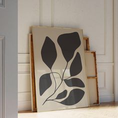 a black and white framed art piece on the floor in front of a wall with a door