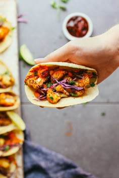 a person holding a taco in their hand with other food on the table behind them