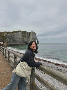 a woman leaning on a fence next to the ocean with cliffs in the back ground