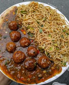 a plate full of spaghetti and meatballs with sauce on the side is being held by someone's hand