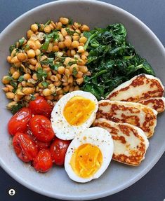 a white plate topped with eggs, tomatoes and spinach next to chickpeas