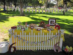 a yellow and white table with pictures on it in the grass next to a fence