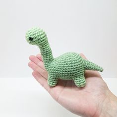 a small green crocheted toy dinosaur in someone's hand on a white background