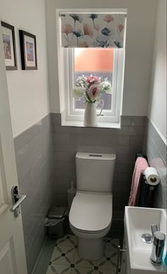 a white toilet sitting in a bathroom next to a window with flowers on the tank