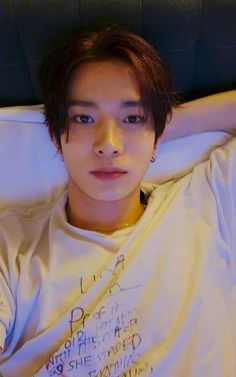 a young man laying on top of a bed wearing a t - shirt with writing on it