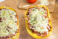 two stuffed squash halves with meat and cheese in them sitting on a cutting board next to a tomato